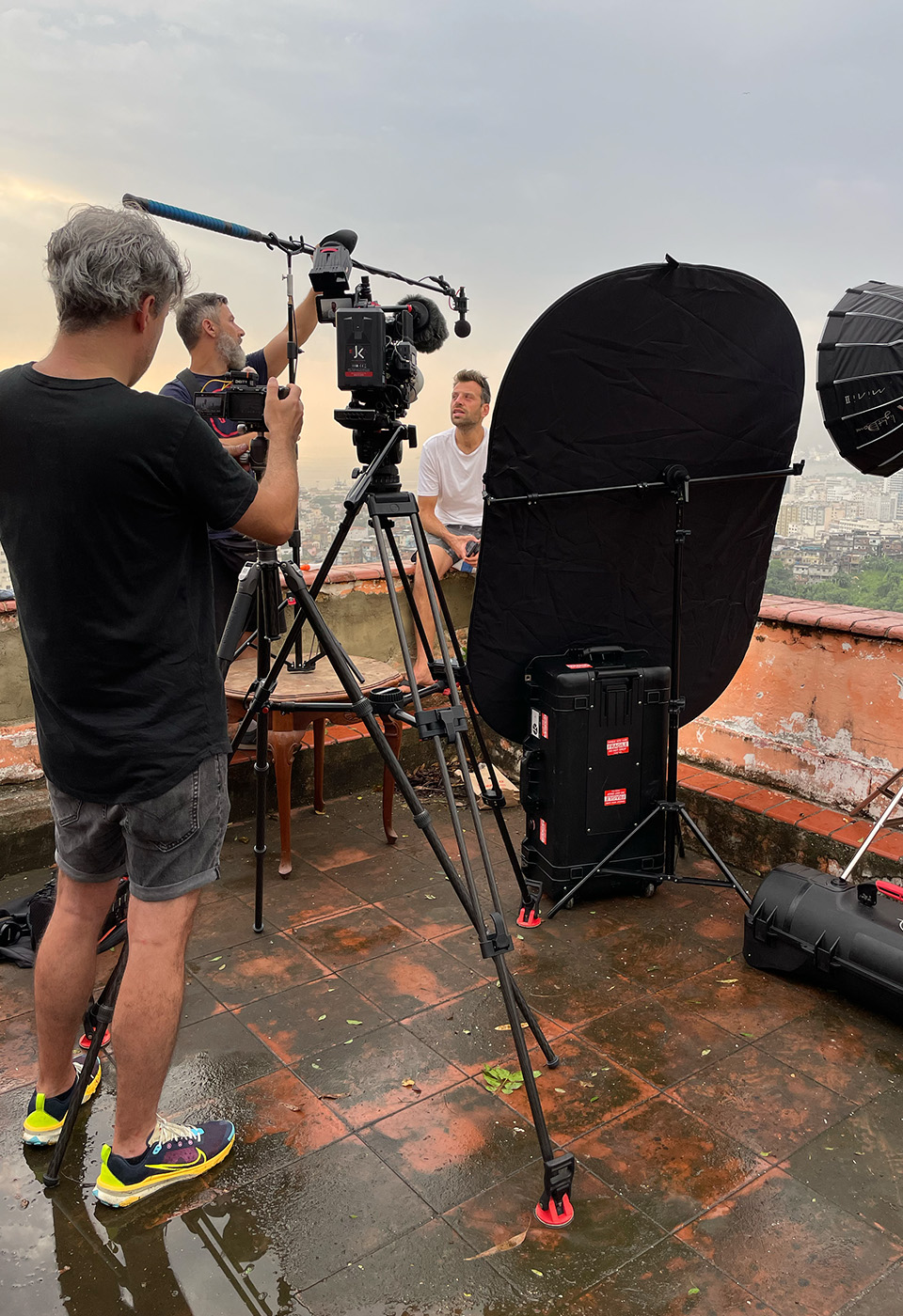Filmteam bei einer Interviewaufnahme auf einer Dachterrasse mit Stadtblick; eine Person sitzt vor der Kamera, während das Team Beleuchtung und Tontechnik arrangiert.